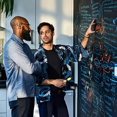 two men discussing work over a blackboard